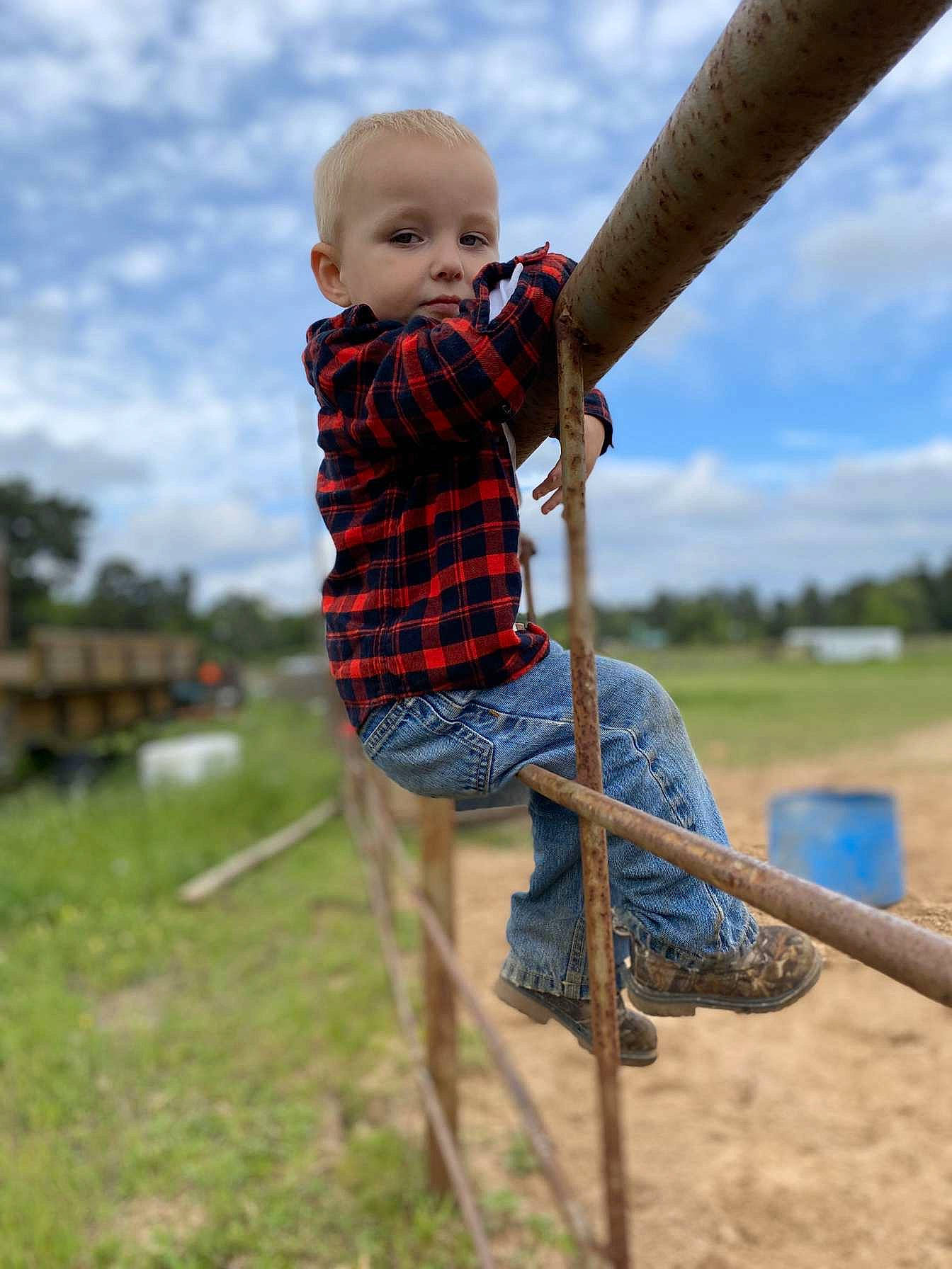 Kooper is registered to the contest to win money with this photo: baby_toddler_clothing, cloud, electric_blue, fun, grass, grassland, happy, leisure, outdoor_play_equipment, pattern, people_in_nature, person, play, playground, recreation, sitting, sky, swing, tartan, toddler