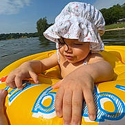 Layana participe au concours pour gagner de l'argent avec cette photo : beach, child, clouds, family, fingers, hand, inflatable_ring, lake, outdoors, playing, portrait, shoreline, sky, smile, sun_hat, sunny, toddler, vacation, water, yellow_float