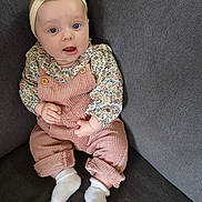Capucine participe au concours pour gagner de l'argent avec cette photo : baby, infant, child, couch, headband, blue_eyes, pink_overalls, floral_shirt, socks, cute, seated, indoors, portrait, soft_lighting, young_child, person, smiling, cozy, comfortable, fashion