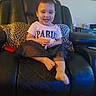 child, toddler, smiling, sitting, portrait, indoors, leather_chair, recliner, leopard_print, pillows, paris_shirt, pink_shirt, skirt, barefoot, toy, living_room, home, furniture, wall_clock, happy