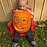 Kaden is registered to the contest to win money with this photo: child, toddler, baby, pumpkin, halloween, jack_o_lantern, outdoor, autumn, grass, fallen_leaves, red_chair, sitting, portrait, face, blond_hair, looking_down, orange, carved_pumpkin, playful, garden