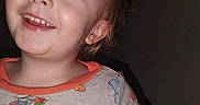 Kaden joined the competition — help win amazing prizes! child, toddler, smiling, happy, portrait, face, eyes, teeth, brown_hair, light_skin, indoor, close_up, pajamas, cartoon_clothing, colorful_clothing, seated, arm, dark_background, flash_photography, casual_photo