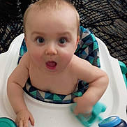 Ivan is registered to the contest to win money with this photo: baby, child, high_chair, toy, indoor, person, seat, furniture, patterned_cushion, blue, skin, hand, expression, face, mouth_open, eyes, young, infant, curious, candid