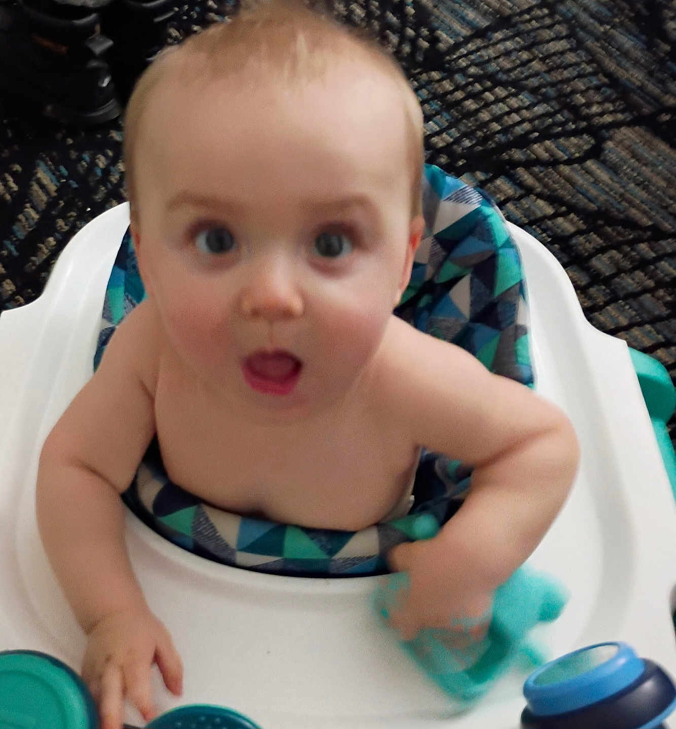 Ivan is registered to the contest to win money with this photo: baby, child, high_chair, toy, indoor, person, seat, furniture, patterned_cushion, blue, skin, hand, expression, face, mouth_open, eyes, young, infant, curious, candid