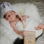 Raphaël participe au concours pour gagner de l'argent avec cette photo : baby, sleeping, chef_hat, wooden_spoon, blanket, basket, cushion, white_fur, infant, soft_texture, nestle, dessert, cozy, resting, cute, newborn, indoor, portrait, peaceful, wrapped