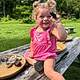 toddler, child, smiling, pink_dress, curly_hair, outdoor, picnic_table, rocks, water, nature, greenery, sunny, happy, play, summer, grass, wood, holding, barefoot, fun