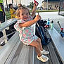 toddler, child, smiling, bleachers, sports_field, baseball, curly_hair, summer_clothing, outdoor, daylight, water_bottle, sports_equipment, backpack, people, concrete, metal, recreation, happy, playful, casual
