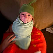 Kasen joined the competition — help win amazing prizes! newborn, baby, infant, swaddled, green_hat, blanket, red_blanket, polka_dots, portrait, face, serious_expression, indoors, warm_lighting, closeup, hand, adult_hand, cuddling, baby_clothing, cozy, family