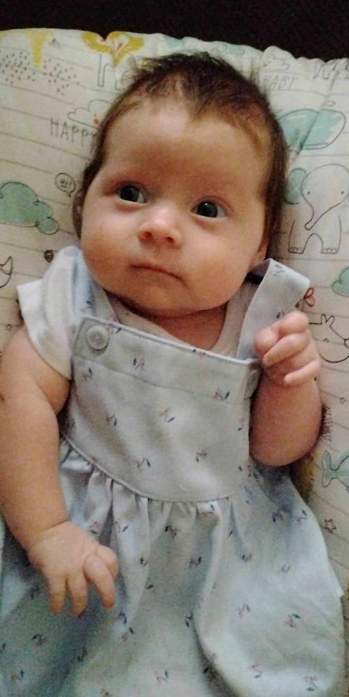 Zoey is registered to the contest to win money with this photo: baby, infant, child, dress, clothing, face, hand, cushion, pattern, animal_print, curly_hair, lying_down, indoor, cute, young, person, closeup, soft_lighting, skin, expression