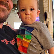 Hayden joined the competition — help win amazing prizes! child, toddler, man, indoor, holding, tshirt, colorful, face, expression, person, adult, ceiling_fan, window, home, living_room, furniture, casual_clothing, portrait, family, parent