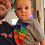 child, toddler, man, indoor, holding, tshirt, colorful, face, expression, person, adult, ceiling_fan, window, home, living_room, furniture, casual_clothing, portrait, family, parent