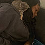 person, kitten, sleeping, couch, indoor, resting, cozy, shoulder, black_hair, casual_clothing, nap, furry_pet, domestic_animal, relaxation, soft_lighting, closeup, quiet, warm, companion, calm