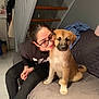 woman, glasses, puppy, dog, couch, stairs, indoor, home, smile, black_clothing, brown_dog, pet, affection, seated, blanket, floor, casual, relaxed, human, furniture