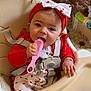 baby, high_chair, comb, headband, bow, red_clothing, white_clothing, heart_pattern, infant, chewing, indoor, kitchen, floor_tiles, cardboard_box, baby_toy, strap, sitting, cute, child, person