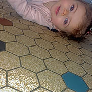 Shelby participe au concours pour gagner de l'argent avec cette photo : amused, baby, cabinet, child, curious, expression, face, floor, hair, hand, head, indoor, kitchen, lying_down, pattern, person, pink_clothing, skin, tile, young_child