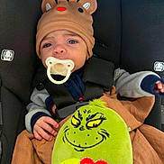 Maxamus joined the competition — help win amazing prizes! baby, child, car_seat, pacifier, reindeer_hat, plush_toy, grinch, blanket, clothing, seatbelt, infant, cute, face, expression, indoors, person, smile, hand, toy, cozy