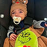 baby, child, car_seat, pacifier, reindeer_hat, plush_toy, grinch, blanket, clothing, seatbelt, infant, cute, face, expression, indoors, person, smile, hand, toy, cozy