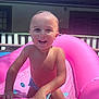 child, toddler, smiling, water, pool, inflatable_toy, pink, sunlight, outdoor, summer, happy, play, skin, hand, face, backyard, water_droplets, fun, daytime, climbing