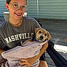 Bron is registered to the contest to win money with this photo: girl, glasses, braces, smile, puppy, dog, towel, outdoor, porch, chair, casual_clothing, nashville_shirt, shorts, human, pet, happy, summer, daylight, relaxation, friendship