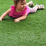 Alyna a rejoint le concours — aidez-le/la à gagner de superbes lots ! toddler, child, grass, artificial_grass, pink_clothing, leggings, shoes, outdoor, smiling, face, hair_ponytail, playful, crawling, skin, person, baby, young_child, daylight, wall, garden