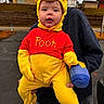 Blakely joined the competition — help win amazing prizes! child, toddler, costume, winnie_the_pooh, yellow, red, cute, outdoor, person, adult, hoodie, holding, parking_lot, buildings, overcast, toy, face, expression, playful, clothing