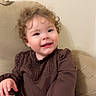 toddler, child, smiling, curly_hair, brown_clothing, diaper, sitting, couch, beige, indoor, happy, cute, face, person, infant, young_child, portrait, home, furniture, baby