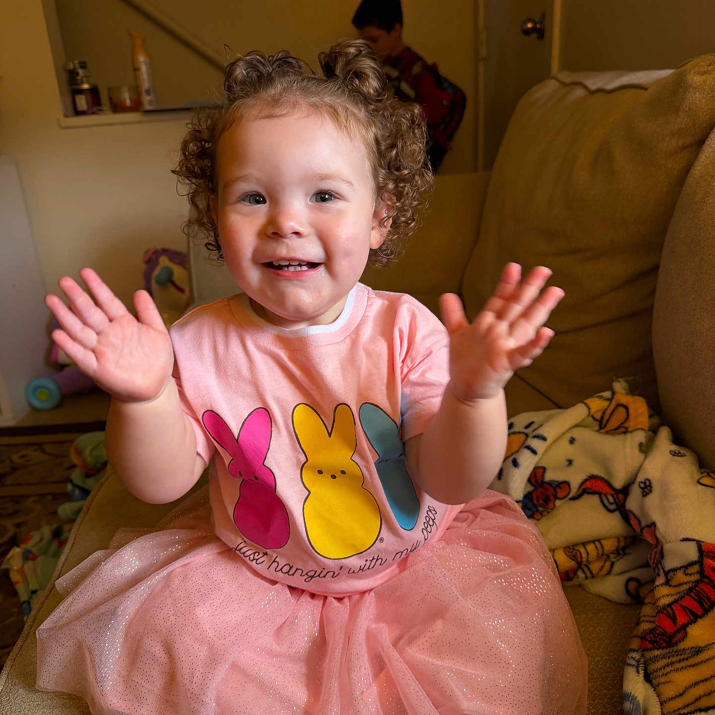 Blakely joined the competition — help win amazing prizes! toddler, child, girl, pink_dress, curly_hair, clapping, couch, blanket, toy, indoor, smiling, happy, person, home, play, background, furniture, casual_clothing, family, curly