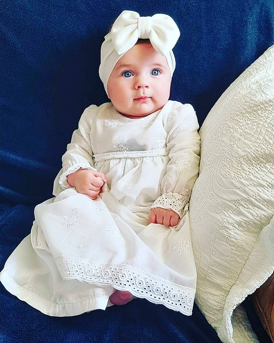 Jeanne participe au concours pour gagner de l'argent avec cette photo : baby, baby_products, baby_toddler_clothing, bridal_accessory, child, comfort, costume_hat, day_dress, dress, embellishment, face, fashion_accessory, hair_accessory, head, headgear, headwear, linens, peach, person, sitting
