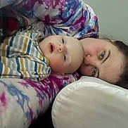 Odin is registered to the contest to win money with this photo: baby, adult, person, face, smile, tie_dye, striped_clothing, indoor, portrait, closeup, candid, relaxed, lying_down, skin, head, cheek, happy, casual, family, bond