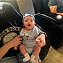 Odin is registered to the contest to win money with this photo: baby, infant, person, clothing, onesie, hat, socks, hand, lap, chair, indoor, floor, jeans, ripped_jeans, black_shirt, expression, wide_eyes, curious, seated, holding