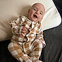 Odin is registered to the contest to win money with this photo: baby, checkered, child, cozy, cushion, cute, dark_background, face, footed_pajamas, happy, indoors, infant, lying_down, pajamas, portrait, relaxed, sleepwear, smiling, white_pillow, young_child