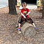 child, boy, red_shirt, spiderman, sandal, wood_log, saddle, outdoor, playground, tree, leaves, wood_chips, pretend_play, nature, casual_clothing, daytime, forest, fun, childhood, recreation