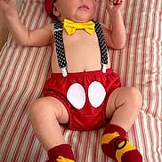 Thomas joined the competition — help win amazing prizes! baby, infant, child, red_hat, yellow_bow_tie, polka_dot_suspender, red_shorts, striped_bedspread, socks, mickey_mouse_theme, lying_down, raised_arms, cute, indoor, portrait, clothing, baby_fashion, soft_lighting, human, young_child