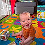 baby, bright, child, colorful, cube_toy, cute, floor, foam_mat, happy, indoor, infant, living_room, orange_clothing, person, play, playtime, sitting, smiling, toy, wooden_box