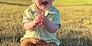 Liam joined the competition — help win amazing prizes! baby, child, happy, smiling, clapping, grass, outdoor, sunlight, shirt, pants, socks, nature, park, daylight, person, cute, young_child, casual_clothing, sitting, face