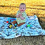 Liam is registered to the contest to win money with this photo: baby, child, smiling, clapping, blanket, toy, bottle, outdoor, grass, sunlight, happy, sitting, cute, infant, playtime, nature, portrait, casual_clothing, daylight, play