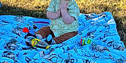 Liam joined the competition — help win amazing prizes! baby, blanket, blue_blanket, bottle, casual_clothing, child, cute, daylight, grass, happy, infant, nature, outdoor, playtime, portrait, sitting, smiling, sunlight, toy, tree