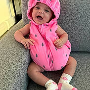 Arya is registered to the contest to win money with this photo: baby, infant, smile, happy, pink_clothing, hood, sock, couch, furniture, indoor, cute, child, portrait, seated, cozy, home, expression, baby_clothes, playful, person