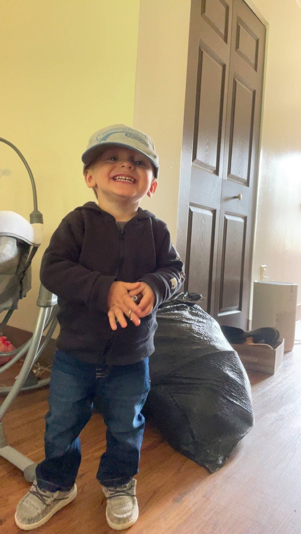 Dawson is registered to the contest to win money with this photo: baseball_cap, cap, child, comfort, denim, door, floor, flooring, fun, hardwood, headwear, home_door, joy, knee, leg, person, sitting, sleeve, smile, standing