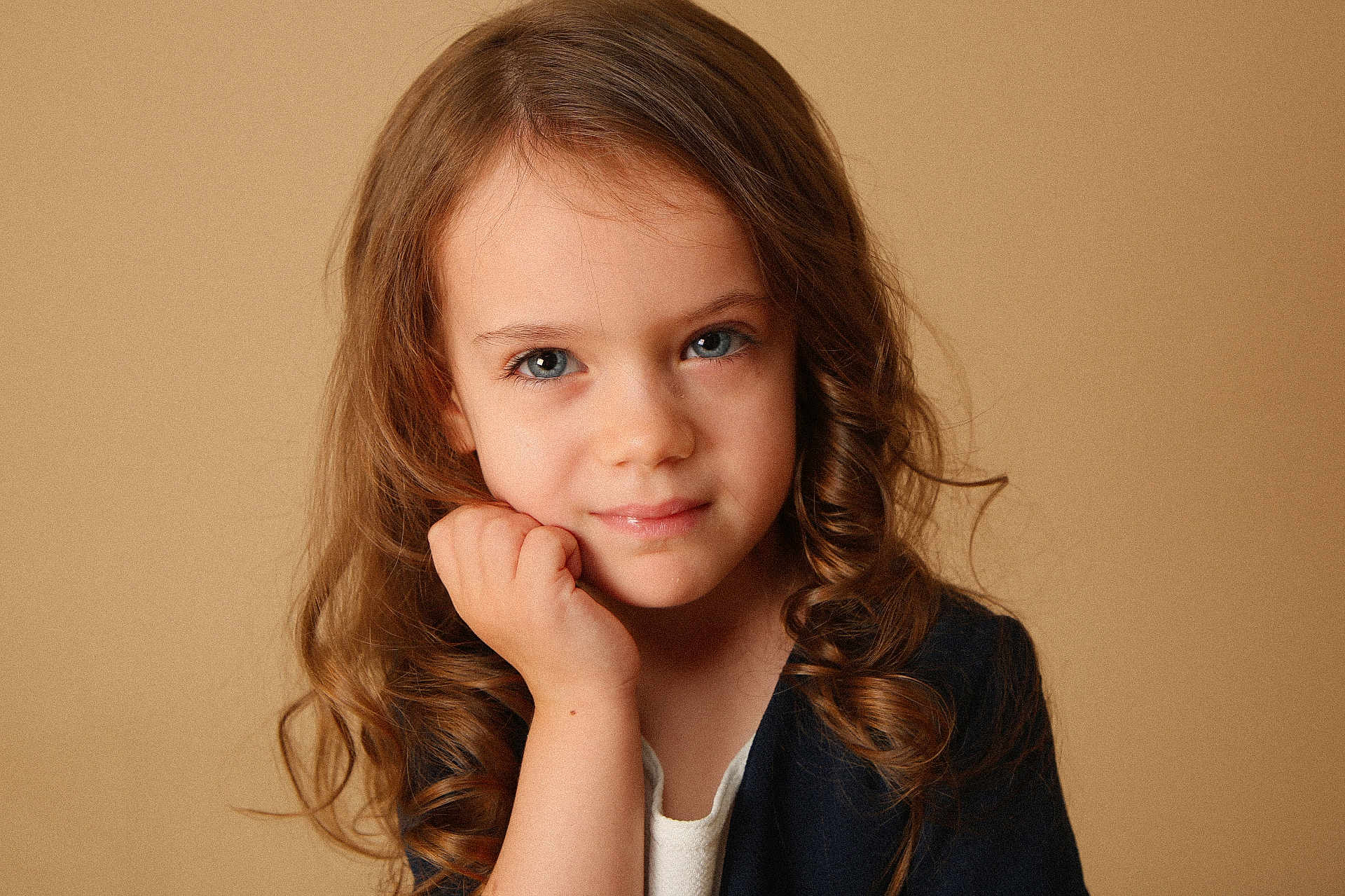 Maëline participe au concours pour gagner de l'argent avec cette photo : child, girl, portrait, face, curly_hair, blue_eyes, hand, expression, closeup, young, person, studio, warm_background, casual_clothing, innocence, soft_lighting, natural, beauty, cute, thinking