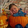 baby, pumpkin, denim_overalls, halloween, spiders, cobwebs, brick_wall, milestone, cute, infant, costume, orange, decorations, holiday, child, portrait, floor, hand, face, celebration