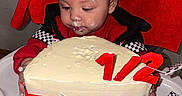 Emerik joined the competition — help win amazing prizes! baby, child, cake, birthday, party_hat, high_chair, frosting, face_paint, celebration, red_clothing, black_and_white_checkered, candle, half_birthday, table, food, indoor, cute, hands, person, smile