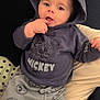 baby, casual, child, clothing, comfort, couch, cute, face, finger_in_mouth, hoodie, indoors, infant, mickey_mouse, pants, person, playful, portrait, sitting, smiling, young_child