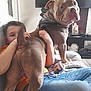 bandana, blanket, brown_dog, casual_clothing, child, couch, dog, face, furniture, home, hugging, human, indoor, jeans, living_room, orange_shirt, pet, playful, relaxing, television