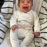 baby, infant, smile, happy, child, white_clothing, striped_blanket, cushion, seated, indoors, cute, person, young_child, face, expression, furniture, soft_texture, portrait, small_hands, footed_pajamas
