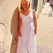 Chelsea a rejoint le concours — aidez-le/la à gagner de superbes lots ! child, girl, white_dress, smile, sunlight, shadow, outdoor, street, wall, sidewalk, blonde_hair, earrings, necklace, casual, summer, happy, standing, portrait, daytime, urban