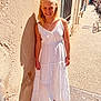 child, girl, white_dress, smile, sunlight, shadow, outdoor, street, wall, sidewalk, blonde_hair, earrings, necklace, casual, summer, happy, standing, portrait, daytime, urban