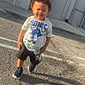 child, toddler, boy, sonic_the_hedgehog, tshirt, shorts, sneakers, outdoor, parking_lot, shadow, sunlight, curly_hair, building, bench, concrete, sidewalk, smiling, standing, daytime, casual_clothing