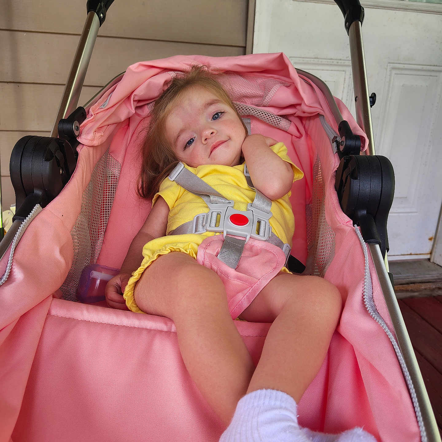 Emerson is registered to the contest to win money with this photo: toddler, stroller, pink, yellow_outfit, socks, child, baby, seatbelt, porch, door, relaxed, curious, infant, outdoor, baby_carriage, person, casual, comfort, young_child, baby_girl