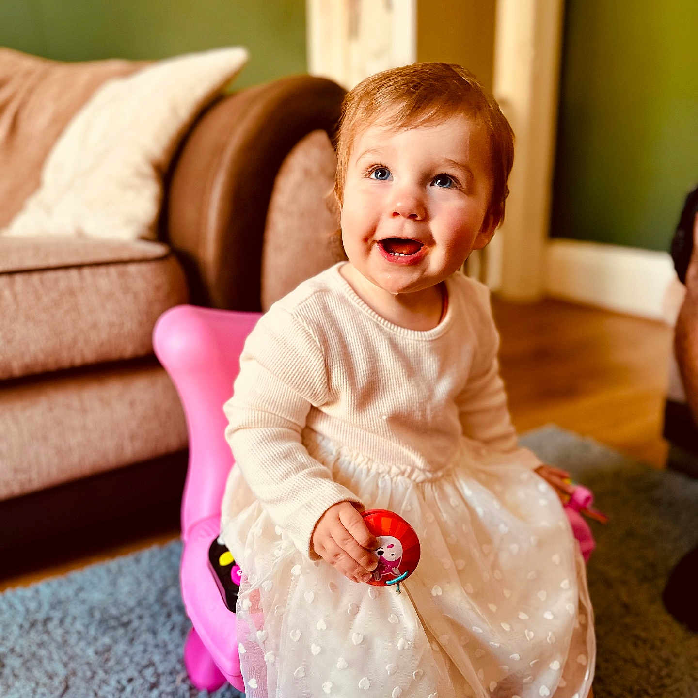 Daisy is registered to the contest to win money with this photo: baby, carpet, child, couch, cute, floor, furniture, happy, home, indoor, light, person, pink_chair, playful, portrait, sitting, smiling, toddler, toy, white_dress
